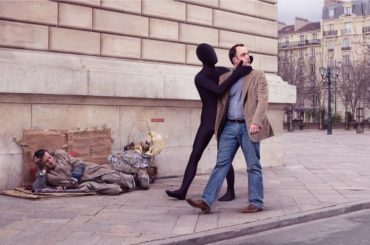 A couple embracing on a city street as a person sleeps rough nearby