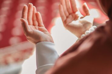 Two open hands raised in prayer, lit in warm red light