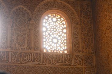 Sunlight through a latticed arched window set in an ornately carved Andalusian plaster wall