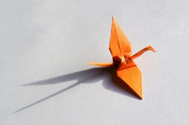 An orange origami crane casting a long shadow on a grey surface