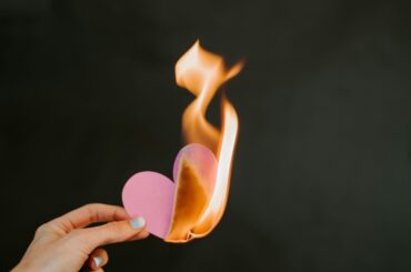 A hand holding a pink paper heart as it burns